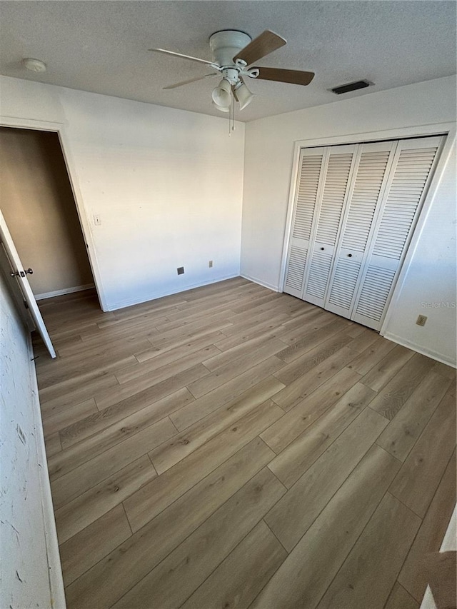 unfurnished bedroom with a closet, visible vents, a ceiling fan, a textured ceiling, and wood finished floors