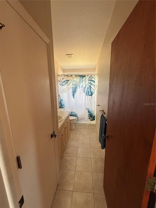 bathroom with curtained shower, toilet, vanity, a textured ceiling, and tile patterned floors