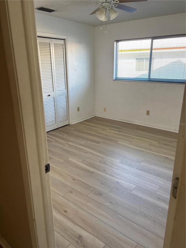 spare room featuring light wood-style floors, ceiling fan, visible vents, and baseboards