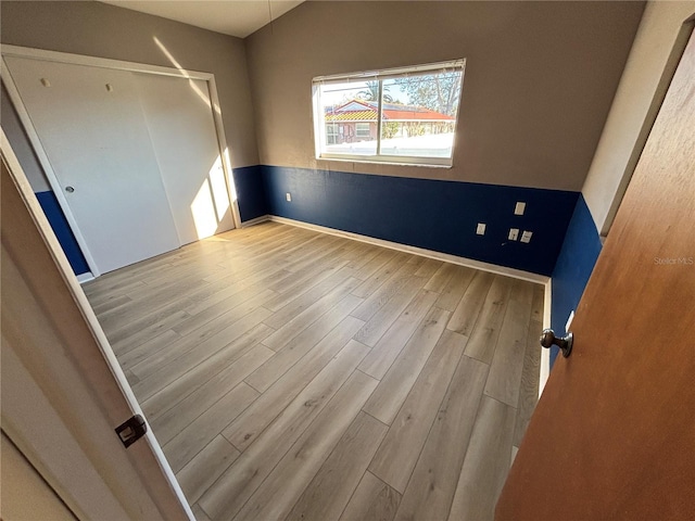 unfurnished bedroom with lofted ceiling, baseboards, and wood finished floors