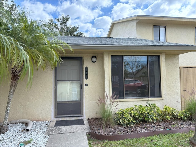 view of exterior entry featuring roof with shingles and stucco siding