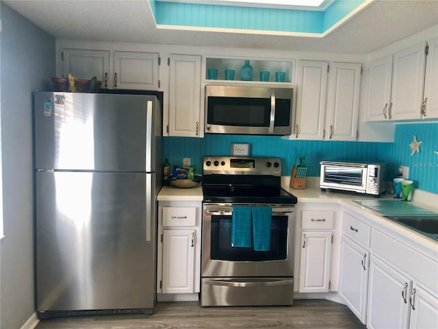 kitchen featuring a toaster, stainless steel appliances, light countertops, dark wood-type flooring, and white cabinetry