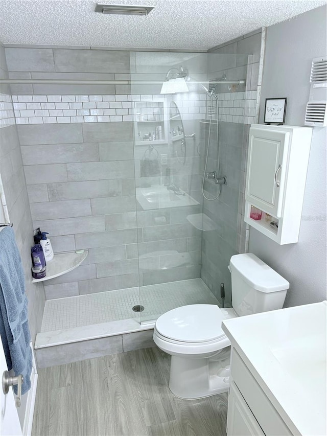 bathroom featuring toilet, wood finished floors, a tile shower, a textured ceiling, and vanity