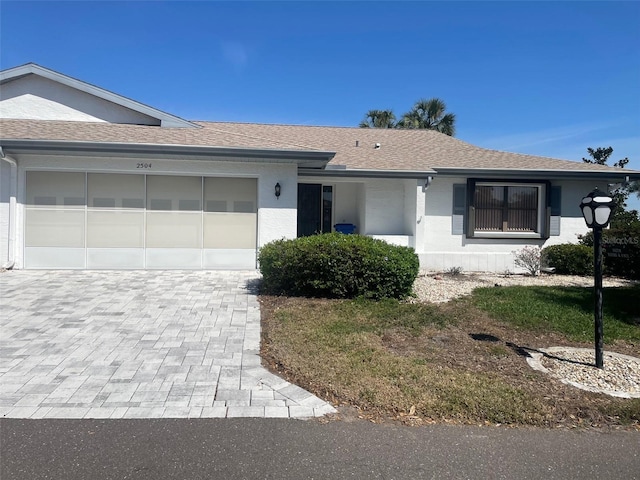 single story home featuring a garage, roof with shingles, decorative driveway, and stucco siding