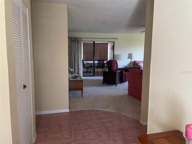 hall with a textured ceiling, carpet, tile patterned flooring, and baseboards