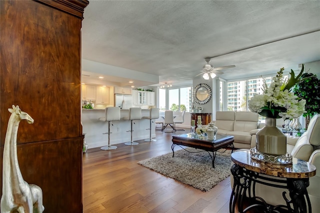 living room with ceiling fan, a textured ceiling, and wood finished floors