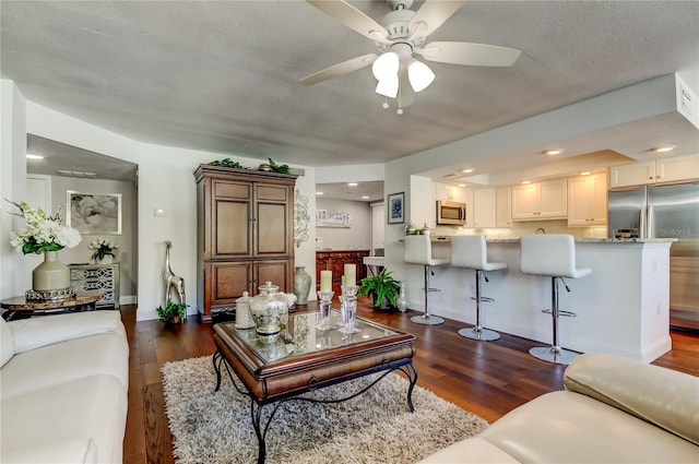 living room featuring ceiling fan, a textured ceiling, baseboards, and dark wood-style flooring