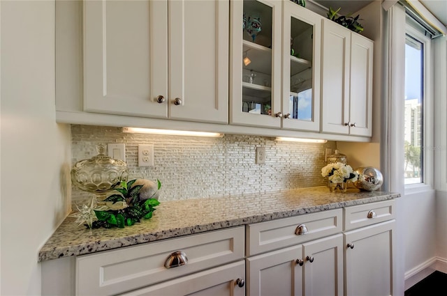 interior space with backsplash, glass insert cabinets, and white cabinetry