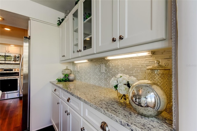 kitchen featuring decorative backsplash, appliances with stainless steel finishes, glass insert cabinets, white cabinetry, and light stone countertops