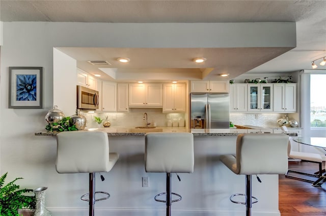 kitchen featuring white cabinetry, appliances with stainless steel finishes, a raised ceiling, dark wood finished floors, and glass insert cabinets