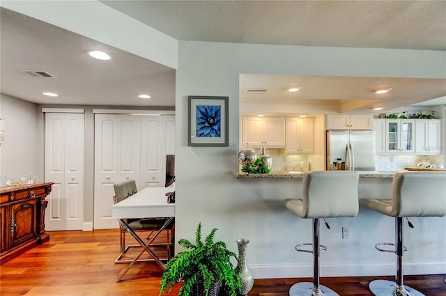 kitchen featuring a breakfast bar area, visible vents, white cabinets, light wood-type flooring, and stainless steel refrigerator with ice dispenser