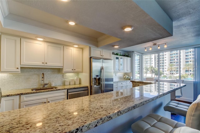 kitchen featuring a raised ceiling, ornamental molding, appliances with stainless steel finishes, a kitchen breakfast bar, and a sink