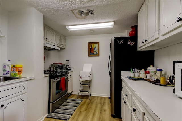 kitchen featuring light wood-style flooring, under cabinet range hood, visible vents, light countertops, and stainless steel electric range oven