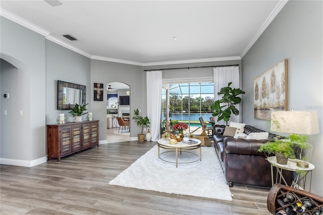 living room featuring baseboards, visible vents, arched walkways, ornamental molding, and wood finished floors