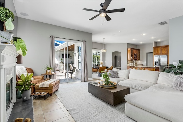 living room with arched walkways, light tile patterned floors, visible vents, a high end fireplace, and ceiling fan