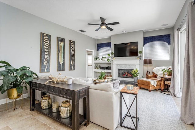 living area featuring visible vents, a ceiling fan, a glass covered fireplace, tile patterned flooring, and baseboards