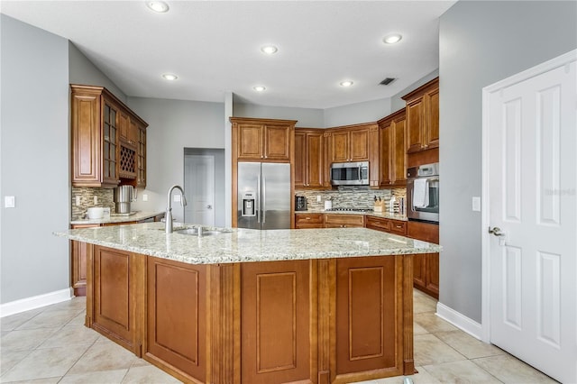 kitchen featuring light stone counters, light tile patterned floors, stainless steel appliances, brown cabinetry, and a sink