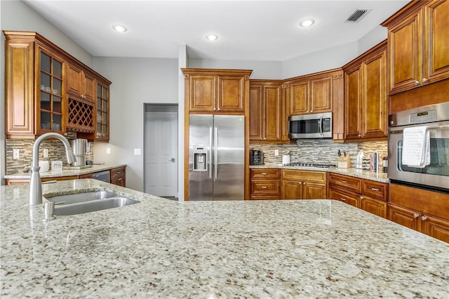 kitchen with appliances with stainless steel finishes, glass insert cabinets, a sink, and light stone countertops