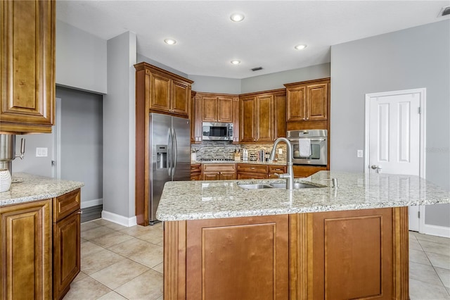 kitchen with stainless steel appliances, tasteful backsplash, brown cabinetry, a sink, and light stone countertops