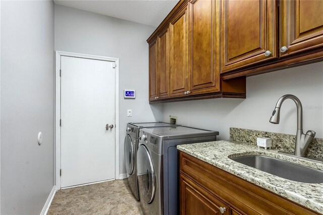 washroom featuring cabinet space, baseboards, a sink, and washing machine and clothes dryer