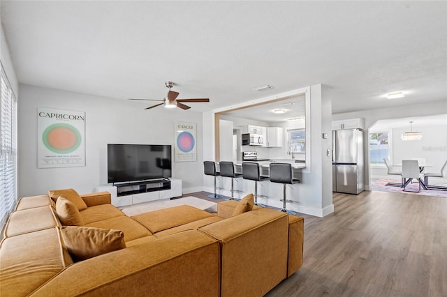 living area with visible vents, baseboards, light wood-style flooring, and a ceiling fan