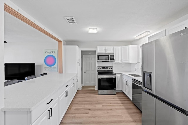 kitchen with light wood finished floors, visible vents, a peninsula, stainless steel appliances, and a sink