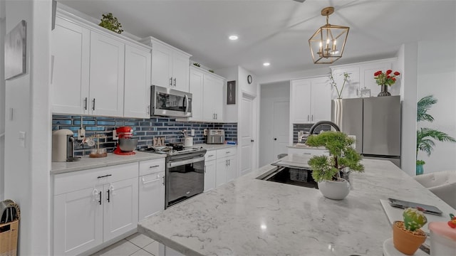 kitchen with decorative backsplash, appliances with stainless steel finishes, decorative light fixtures, light stone countertops, and white cabinetry