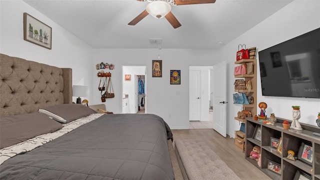 bedroom with a walk in closet, a closet, visible vents, a ceiling fan, and wood finished floors