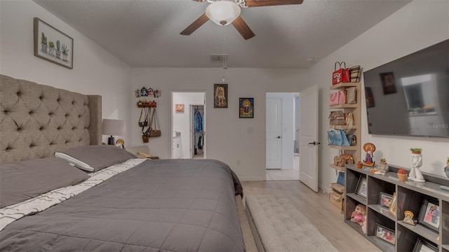 bedroom with a walk in closet, visible vents, light wood-style floors, ceiling fan, and a textured ceiling