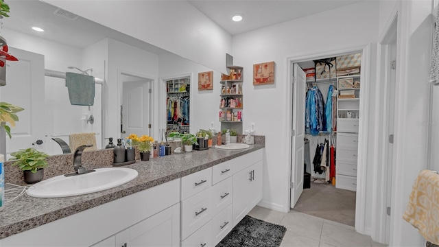 bathroom with a walk in closet, double vanity, visible vents, a sink, and a tile shower