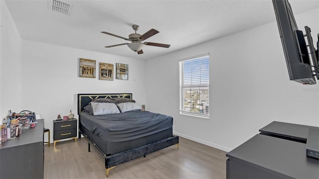 bedroom featuring ceiling fan, wood finished floors, visible vents, and baseboards