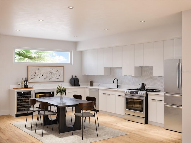 kitchen featuring wine cooler, appliances with stainless steel finishes, white cabinetry, a sink, and light wood-type flooring