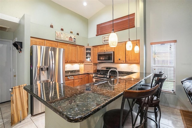 kitchen with brown cabinets, stainless steel appliances, a sink, dark stone counters, and a peninsula