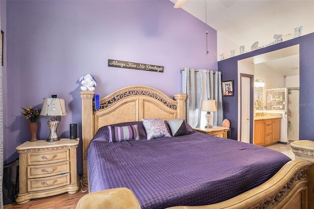 bedroom with ensuite bath, light wood-style flooring, and vaulted ceiling