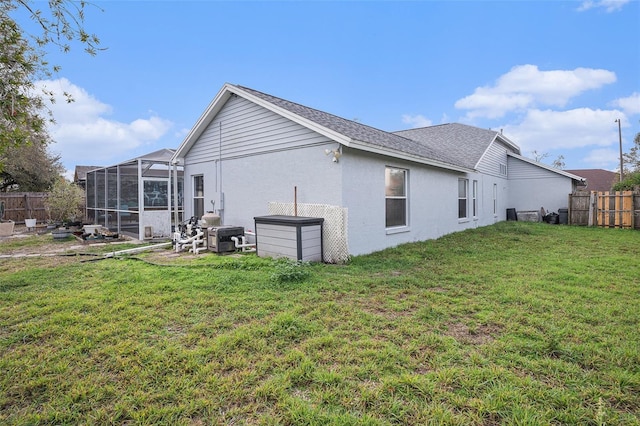 rear view of property featuring glass enclosure, a lawn, fence, and stucco siding