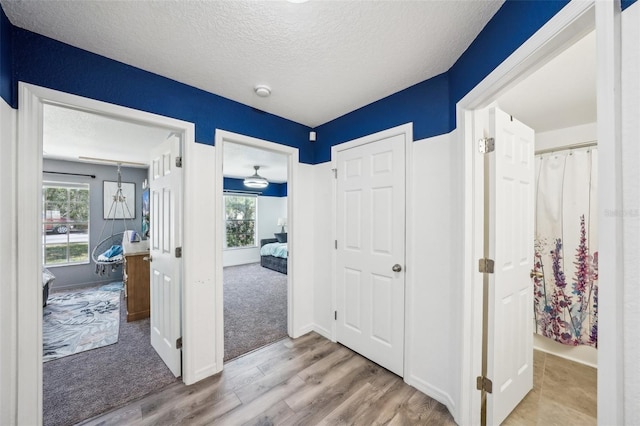 corridor featuring a textured ceiling, wood finished floors, and baseboards