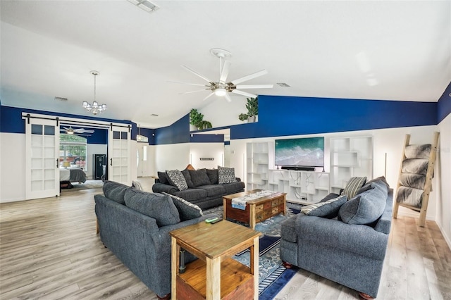 living area featuring a barn door, vaulted ceiling, wood finished floors, and ceiling fan with notable chandelier