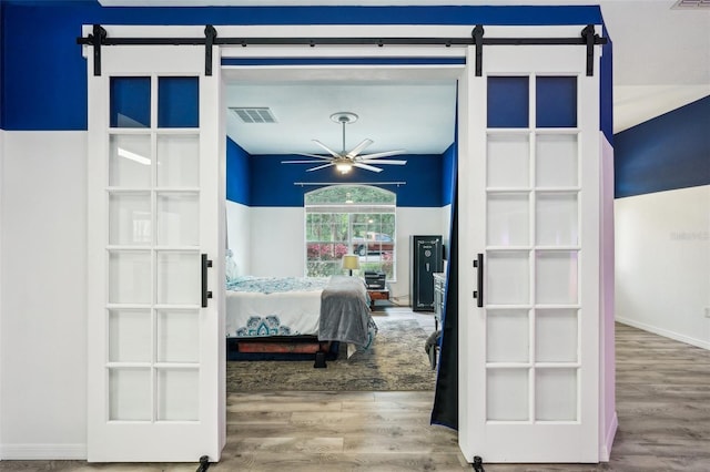 bedroom featuring wood finished floors, visible vents, and a barn door