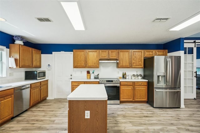 kitchen featuring stainless steel appliances, visible vents, under cabinet range hood, and a barn door