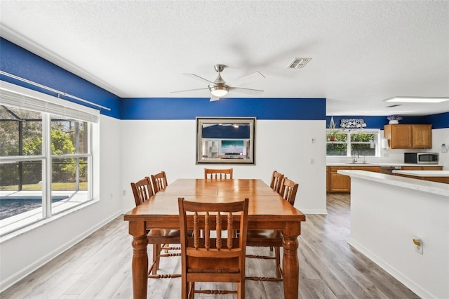 dining space with a ceiling fan, light wood-type flooring, visible vents, and a textured ceiling