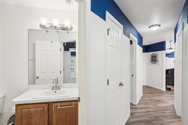 ensuite bathroom with toilet, wood finished floors, ensuite bathroom, a textured ceiling, and vanity