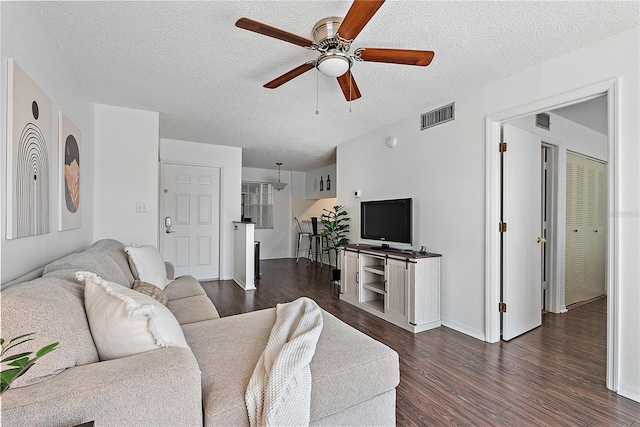 living area with dark wood-type flooring, visible vents, ceiling fan, and a textured ceiling