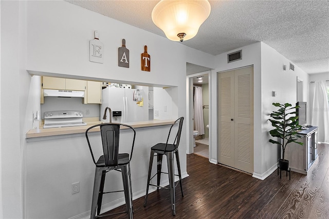 kitchen with dark wood-type flooring, white appliances, visible vents, and under cabinet range hood