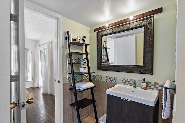 bathroom featuring a textured ceiling, a wainscoted wall, wood finished floors, vanity, and tile walls