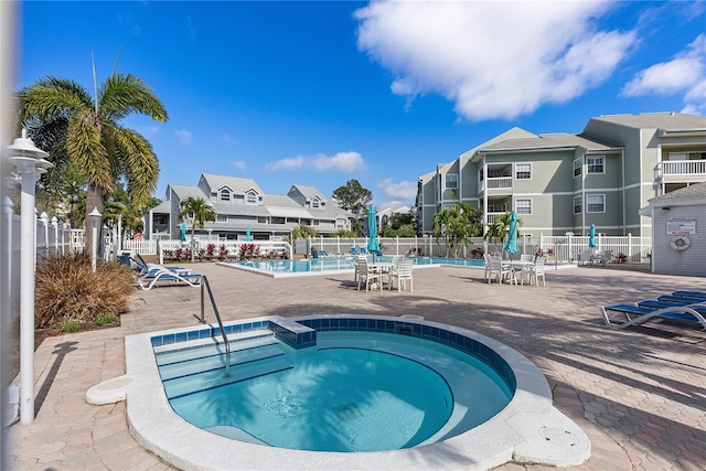 community pool with a patio area, a hot tub, a residential view, and fence