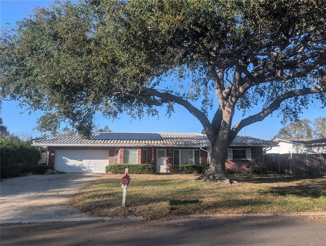 ranch-style house featuring a garage, concrete driveway, fence, roof mounted solar panels, and a front yard