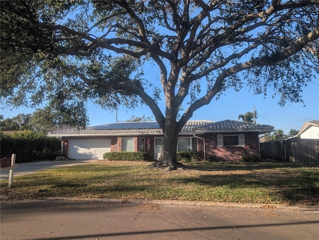 single story home with an attached garage, a front yard, roof mounted solar panels, fence, and driveway