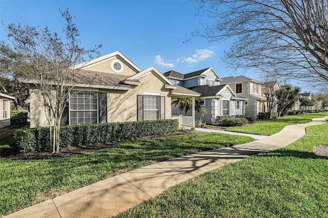 view of front of house with roof with shingles, a front yard, a residential view, and stucco siding