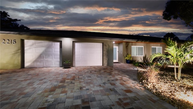 ranch-style house featuring a garage, decorative driveway, and stucco siding