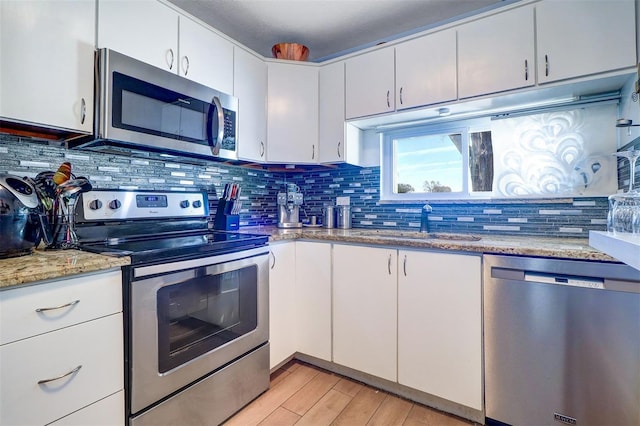 kitchen with light wood finished floors, decorative backsplash, stainless steel appliances, white cabinetry, and a sink